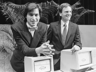 Steve Jobs, a la izquierda, y John Sculley. Sculley se apoya en el ordenador personal Apple "Lisa", sucesor del Macintosh original, sobre el que se apoya Jobs.