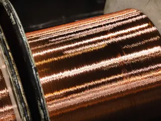 Primer plano de un carrete industrial de alambre de cobre, enrollado de manera uniforme y con reflejos de luz.